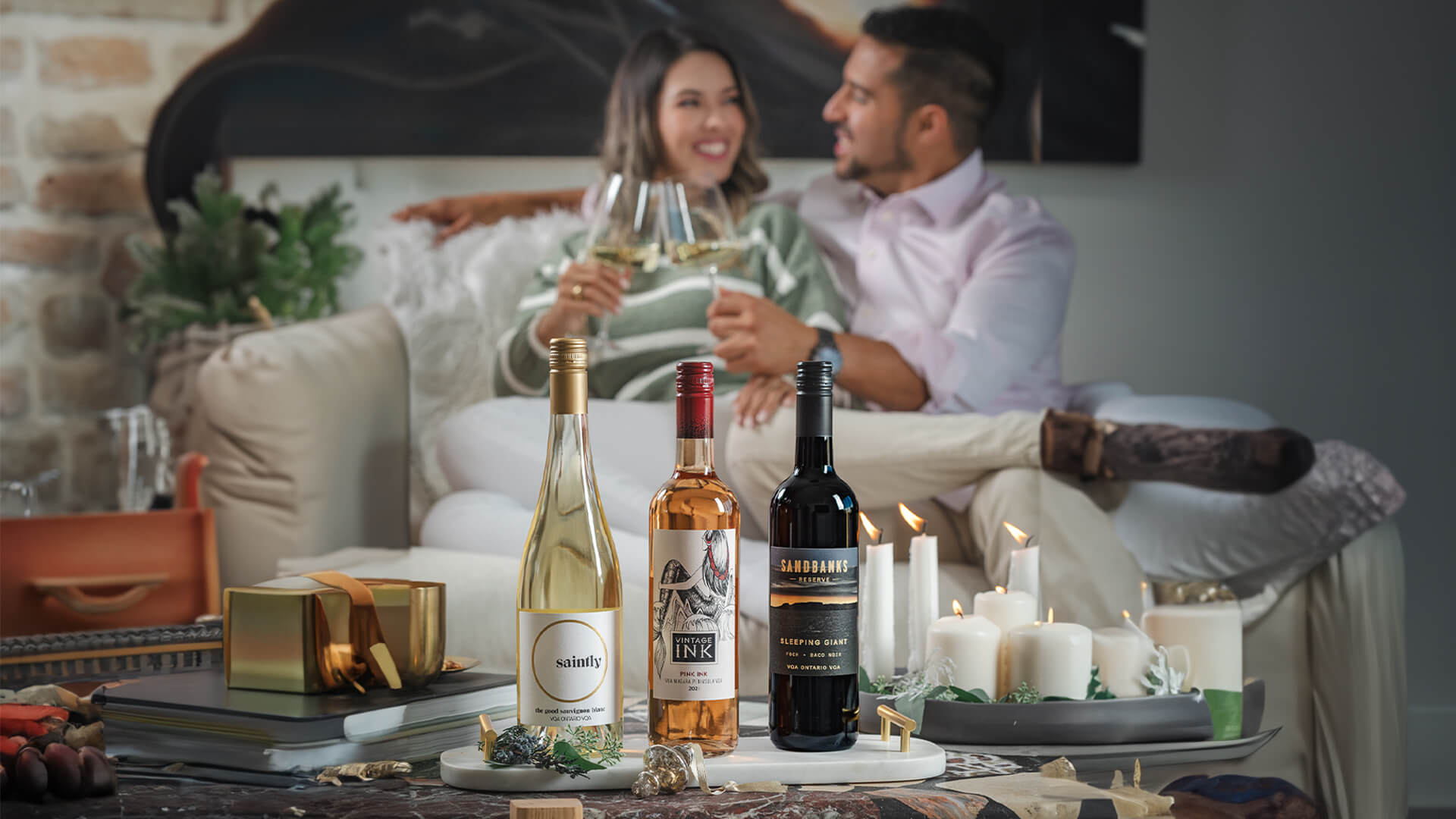 A couple cozied up with a glass of Saintly the Good Sauvignon Blanc, Vintage Ink Rose, and Sandbanks Sleeping Giant Red.